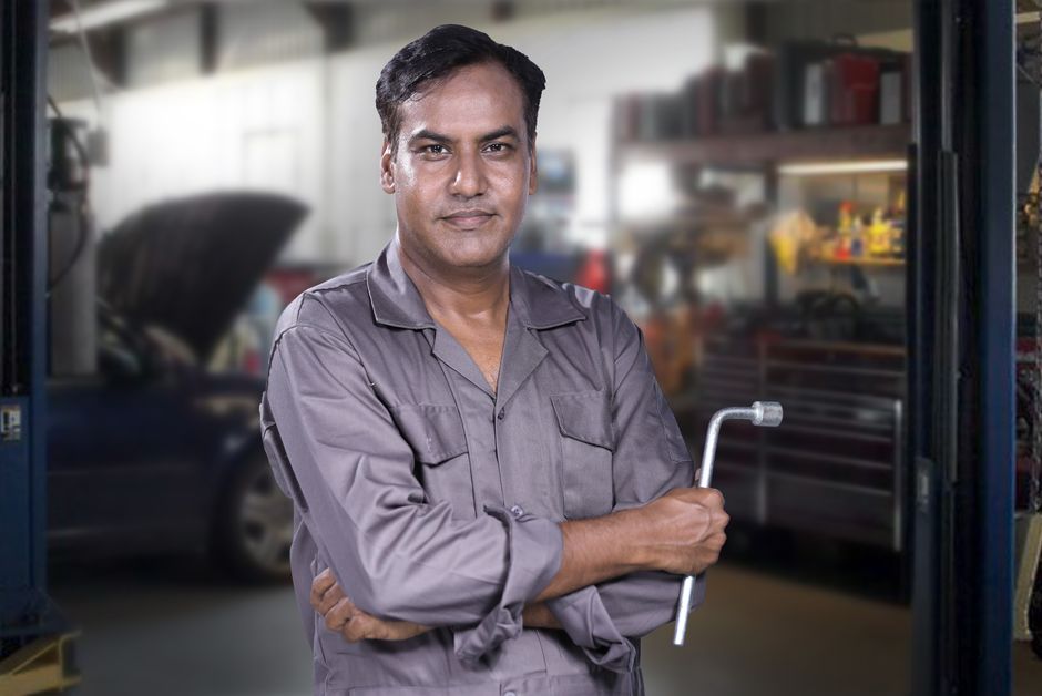Friendly auto mechanic standing next to a vehicle